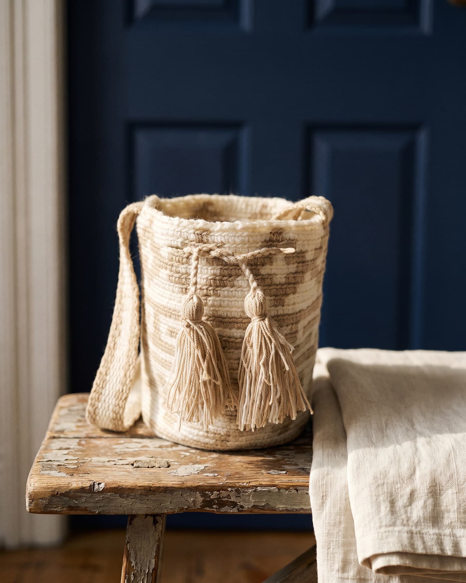 Mochila Geométrica in Creme mit schrägen Bändern in Canela, als Stillleben auf Leinen in warmem Tageslicht.