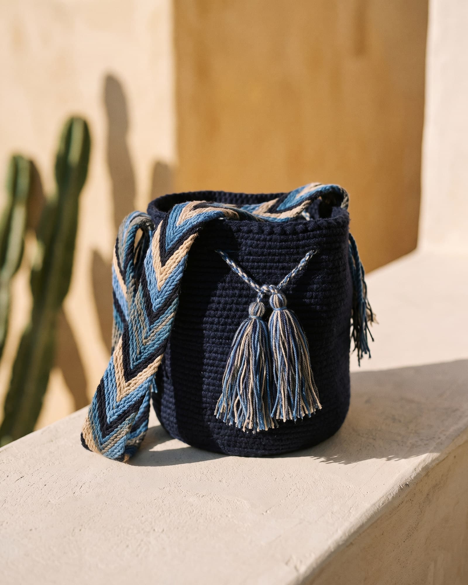 Marineblaue Mochila Lisa als Stillleben auf Leinen in warmem Tageslicht, mit breitem Zickzack-Henkel in Camel, Blau und Schwarz.