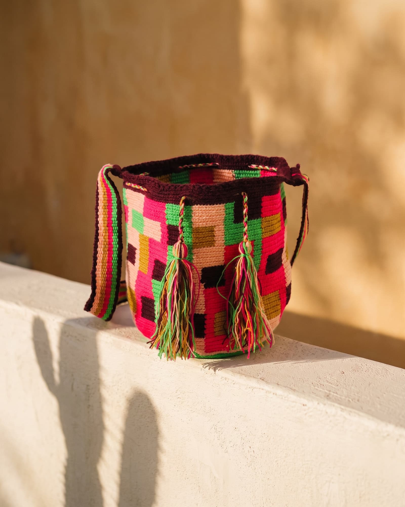 Mochila Mosaico in Neonpink, Pfirsich und Grün mit burgunderrotem Rand, als Stillleben auf Leinen im warmen Tageslicht.