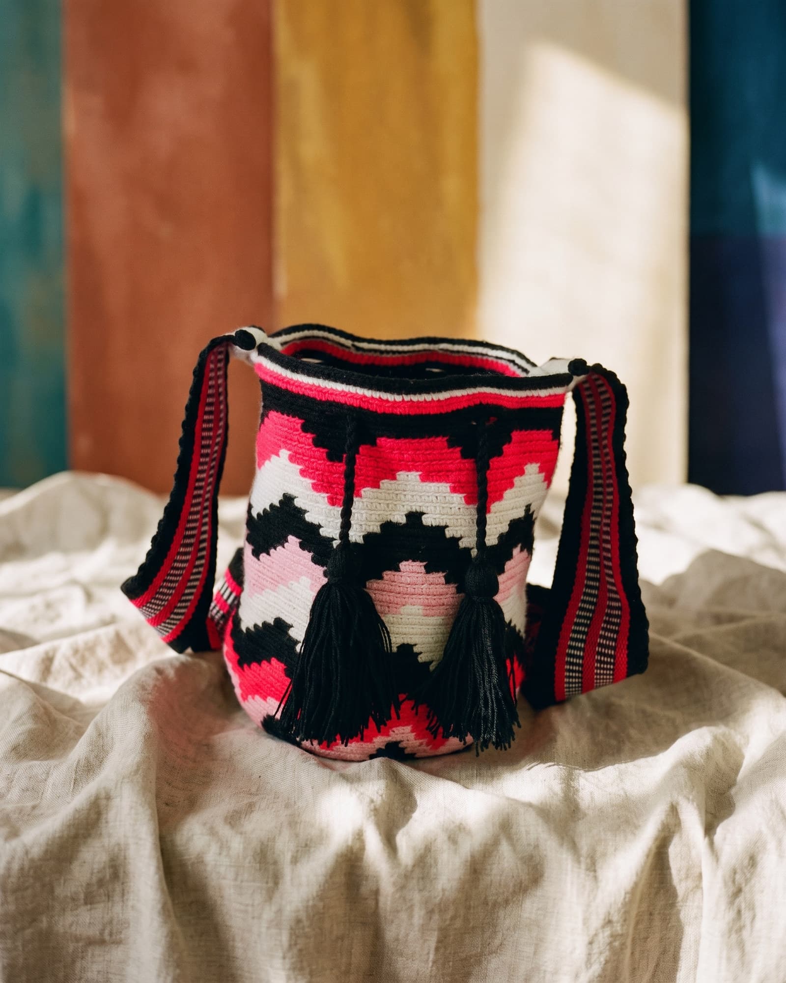 Mochila mit neonrosa, schwarzem und cremefarbenem Zickzackmuster und schwarzen Quasten, auf Leinen liegend im warmen Tageslicht.